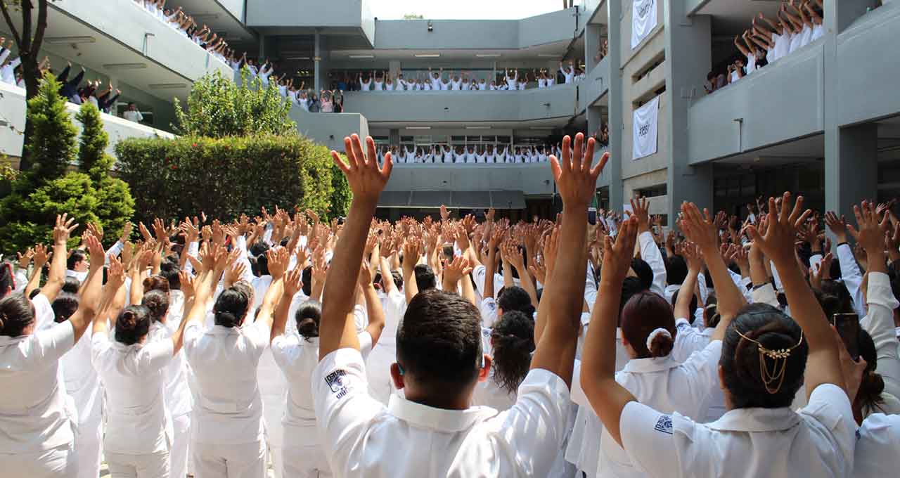 Imagen de la Escuela Nacional de Enfermería y Obstetricia (ENEO). Enfermeros y enfermeras en un acto público levantando las manos.